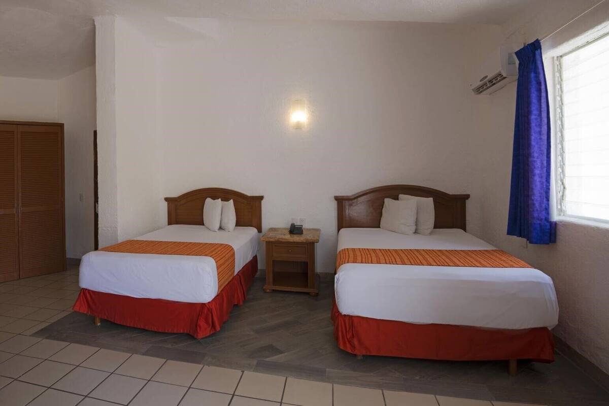 A hotel room with two beds, a nightstand, a wardrobe, and a window with curtains.