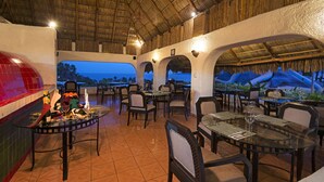 An outdoor dining area with tables and chairs, a bar area with a grill, and a view of the ocean at dusk. - Vista Playa de Oro Manzanillo (Manzanillo)