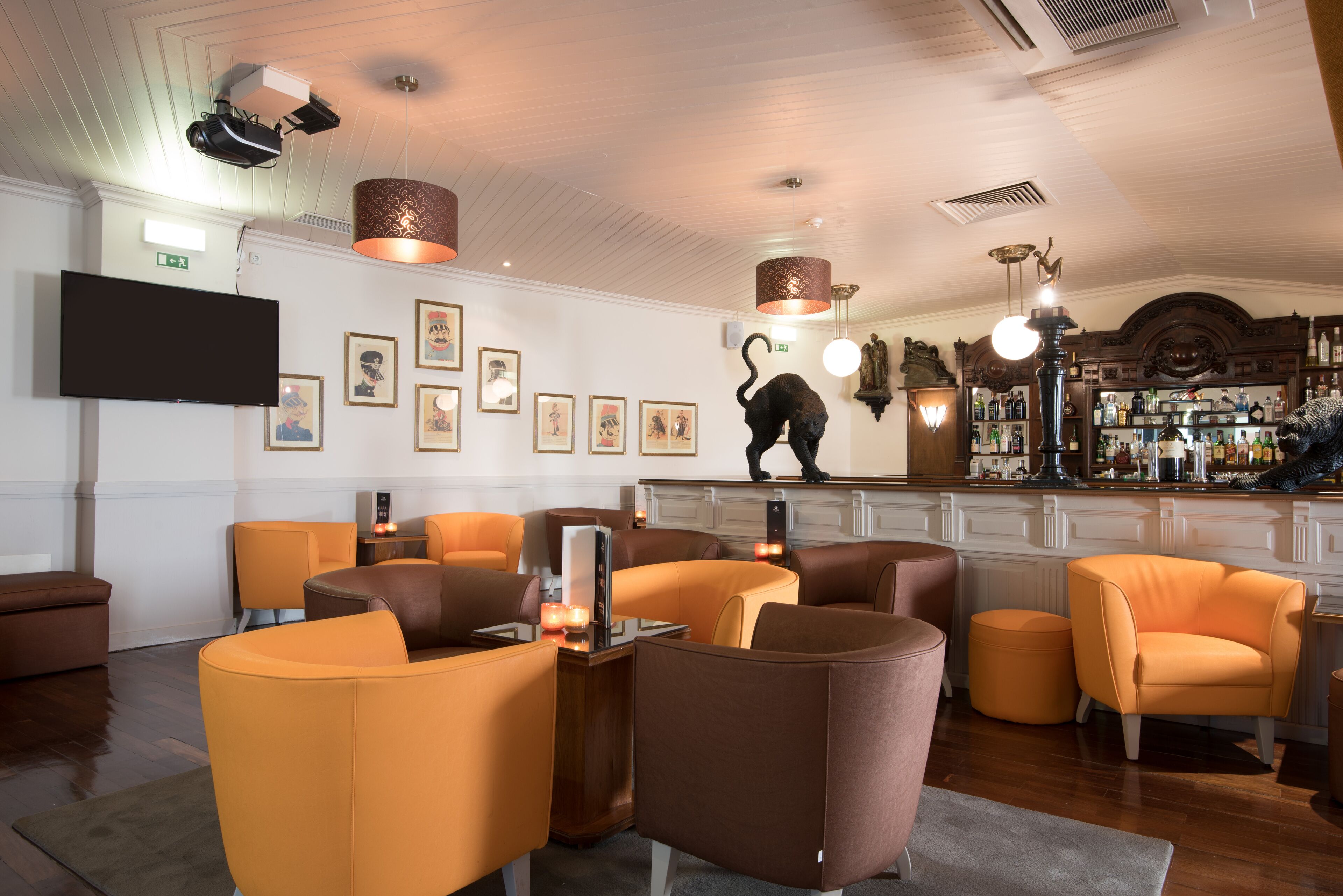 Een barruimte met oranje en bruine zitplaatsen, een flatscreen-tv, ingelijste kunstwerken en een bar gevuld met flessen.