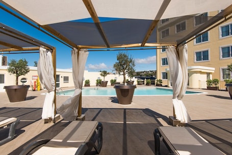 Una piscina al aire libre, sombrillas, sillones reclinables de piscina