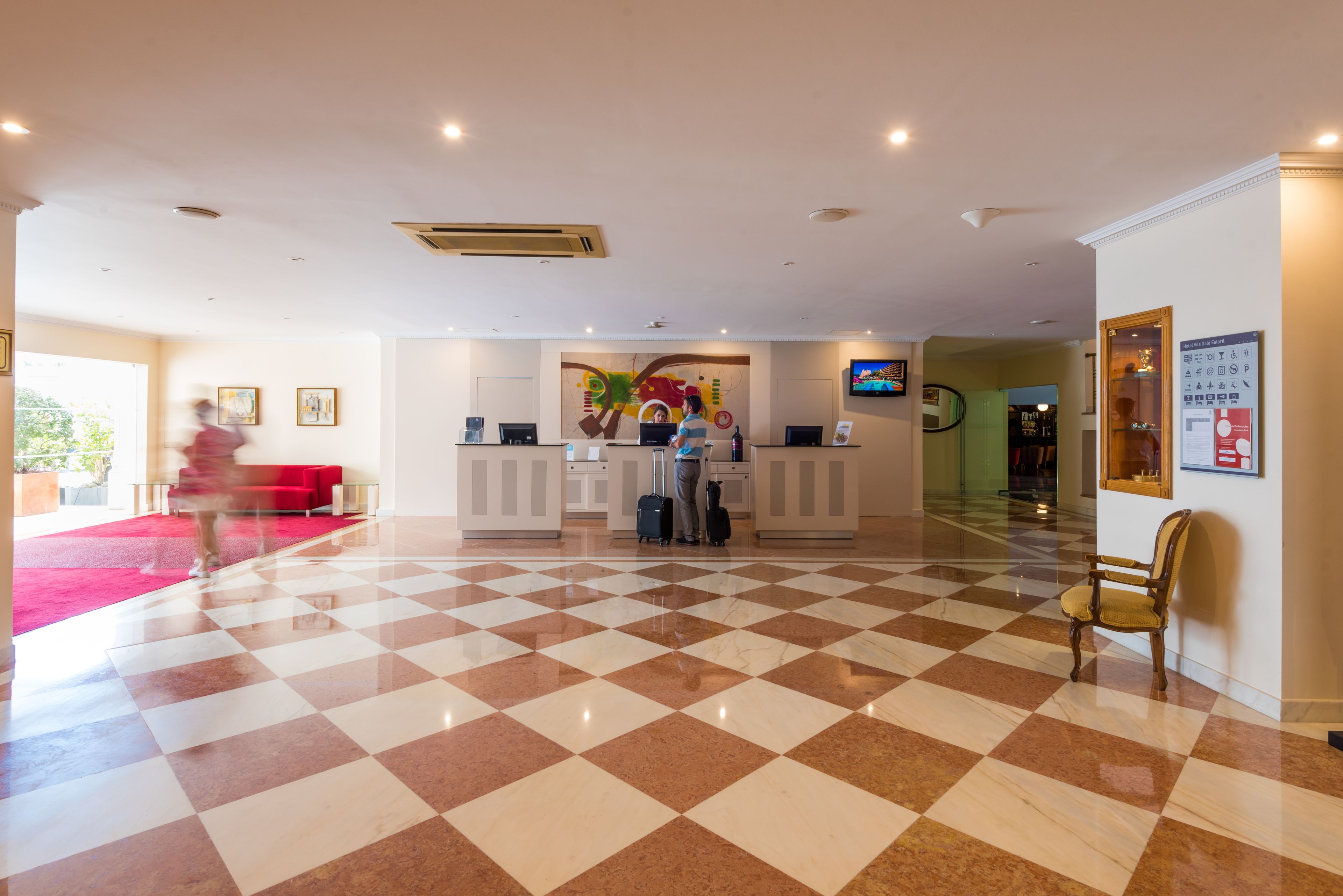 Un vestíbulo de hotel con piso a cuadros, mostrador de recepción y un sofá rojo.