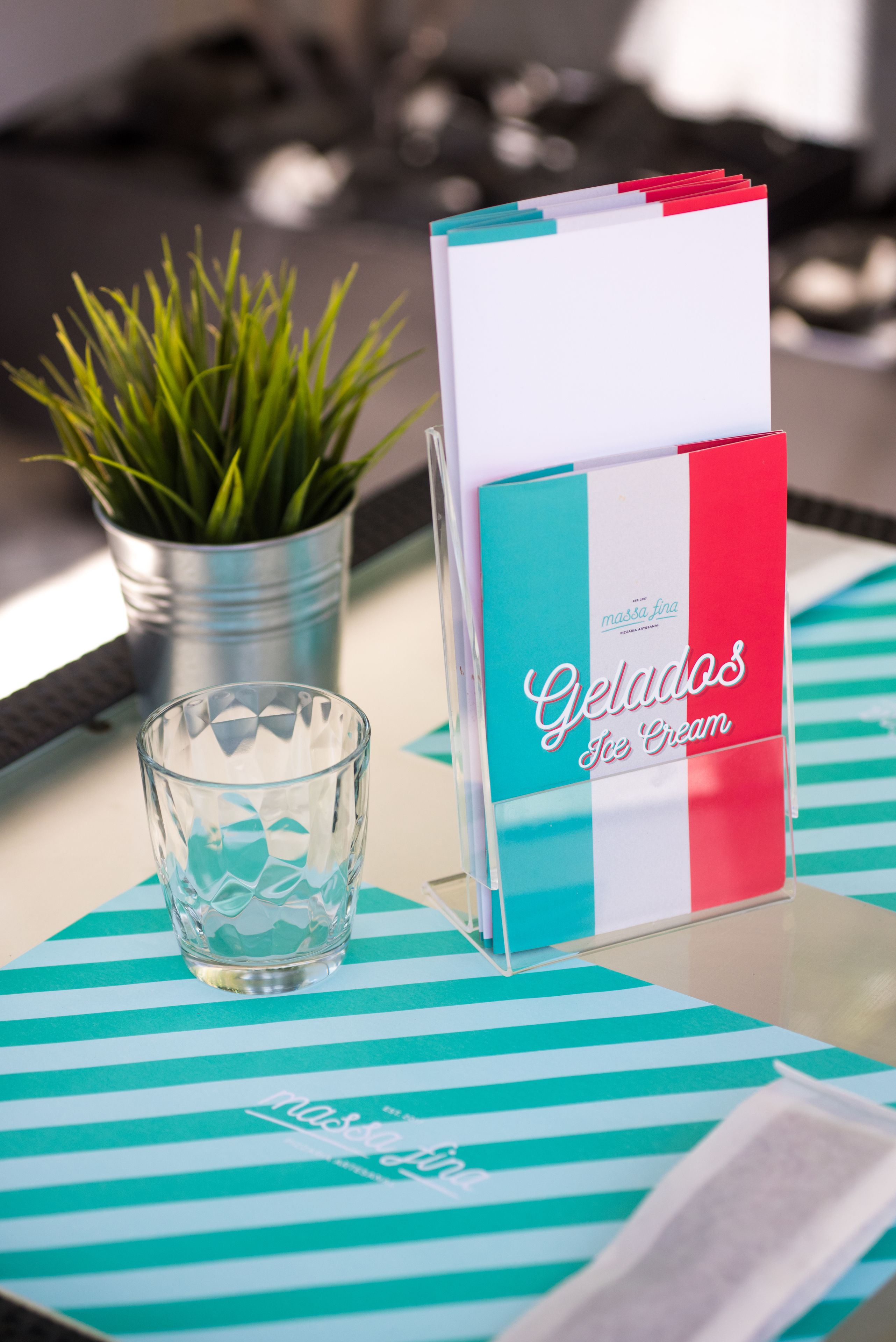 Un présentoir à menu sur lequel est inscrit « Gelados Ice Cream », placé sur une nappe à rayures, avec un verre et une plante en pot en arrière-plan.