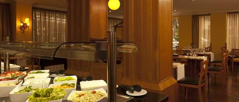 Montaje de bufé con diversos alimentos y un comedor con mesas y sillas.