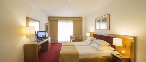 A hotel room with two beds, a desk with a TV, a chair, and a window with curtains.