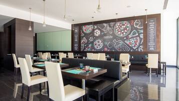 Un restaurante moderno con techo alto, iluminación colgante y una pared con menú en pizarra. Las mesas están dispuestas con sillas, y hay una zona de estar con sofá.