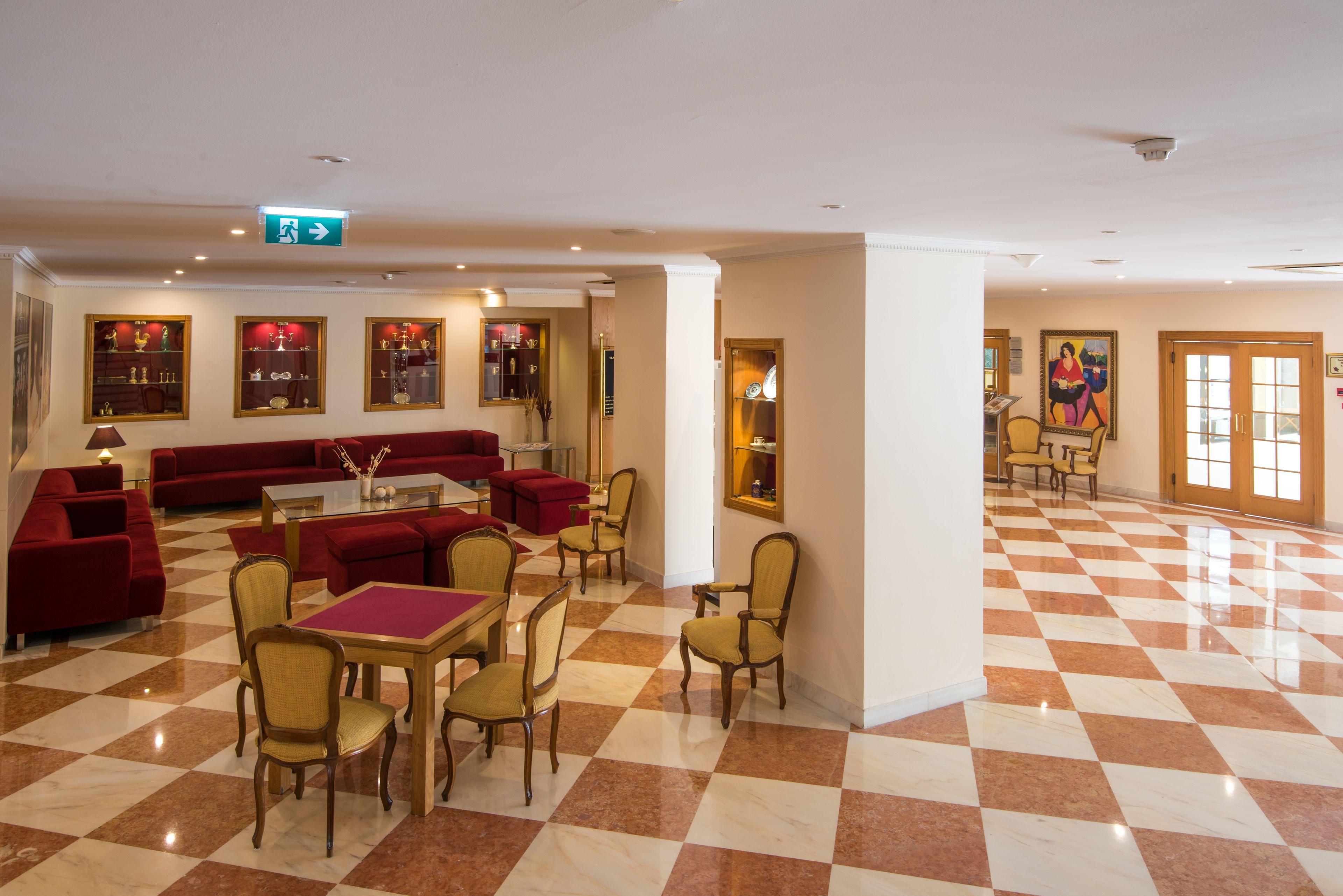 Un hall de hotel con piso a cuadros, sofás rojos y una zona de comedor con mesas y sillas.