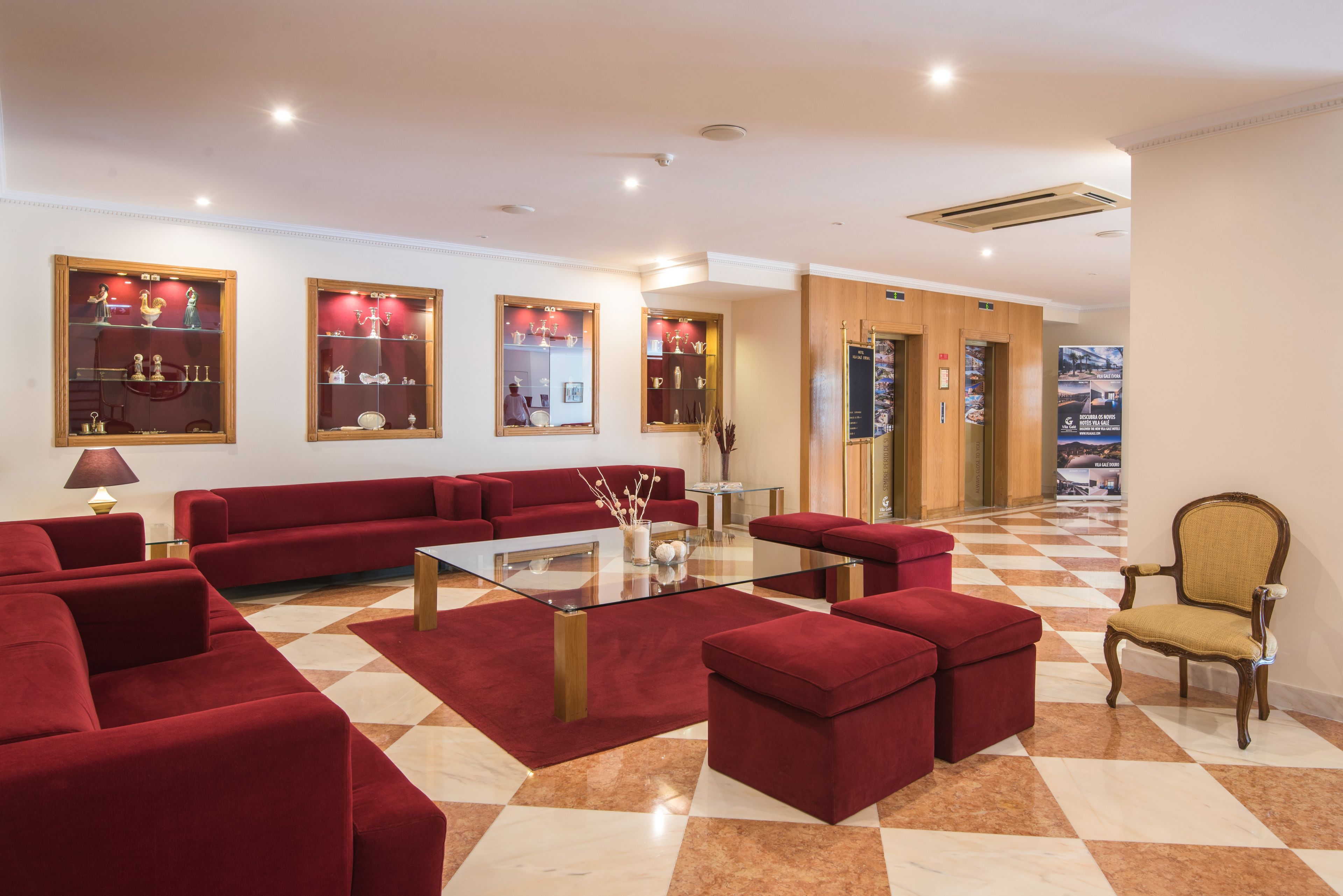Vestíbulo de hotel con sofás rojos, una mesa de centro de vidrio y suelo a cuadros.