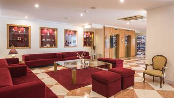 Vestíbulo de hotel con sofás rojos, una mesa de centro de vidrio y suelo a cuadros.