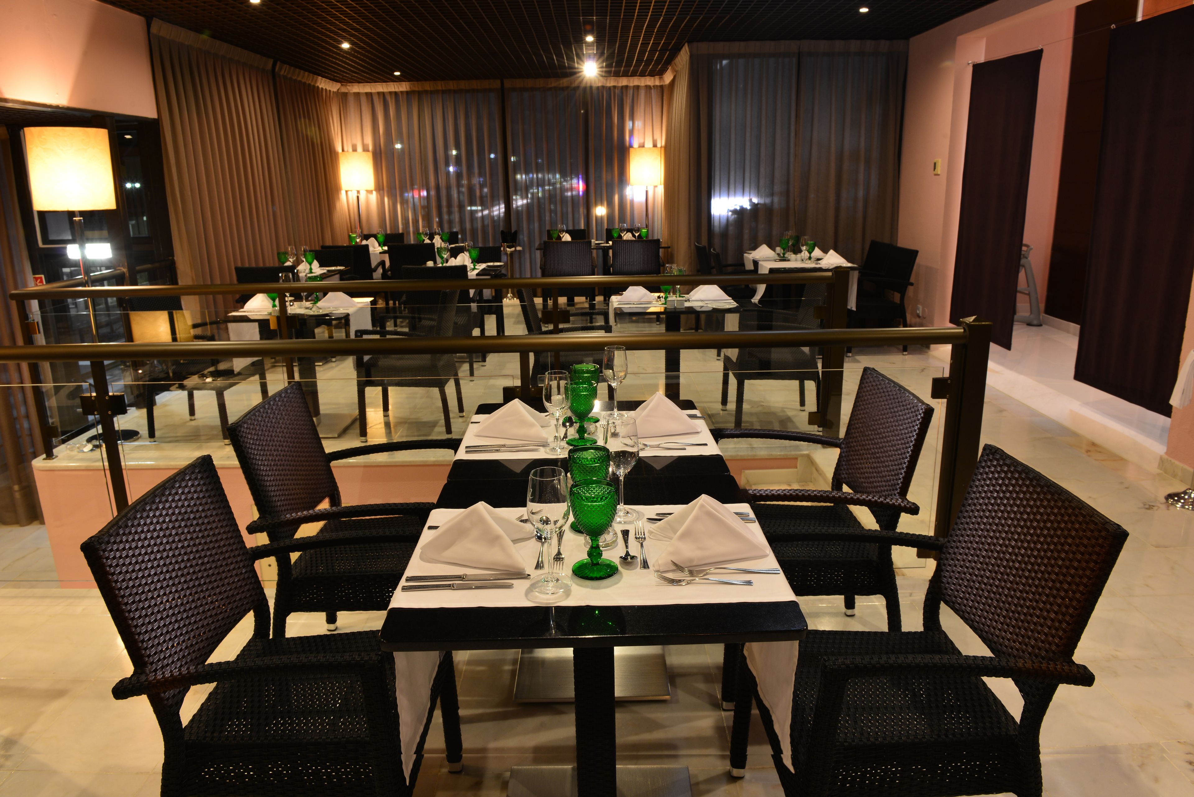 A restaurant with tables set for dining, featuring a central green glass vase and black chairs.