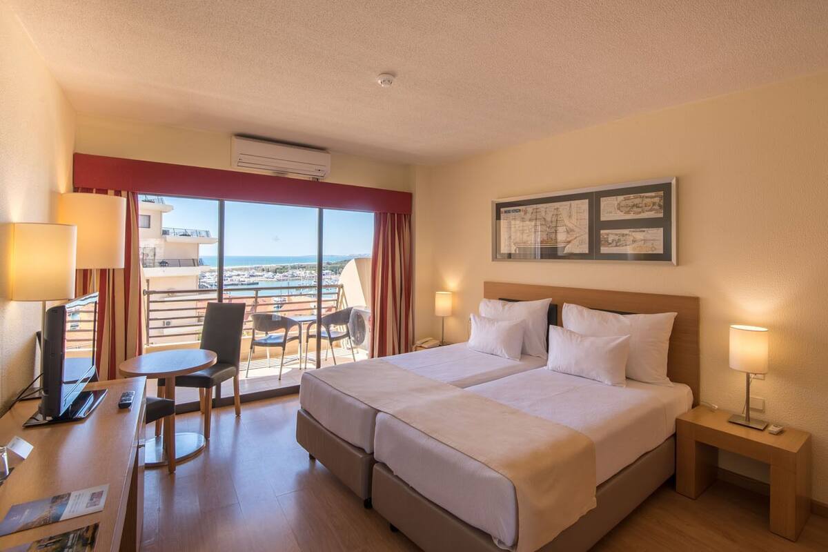 Habitació d'hotel amb llit, taules de nit, escriptori amb cadira, balcó amb vistes i aire condicionat.