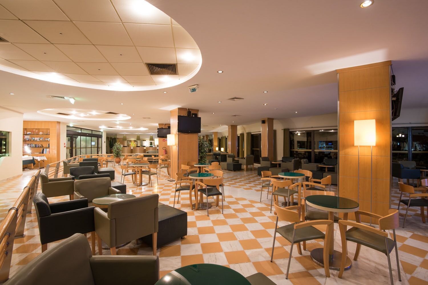 Eine geräumige Lobby mit Schachbrettmuster-Boden, verschiedenen Sitzbereichen und einer zentralen Säule mit Fernseher.