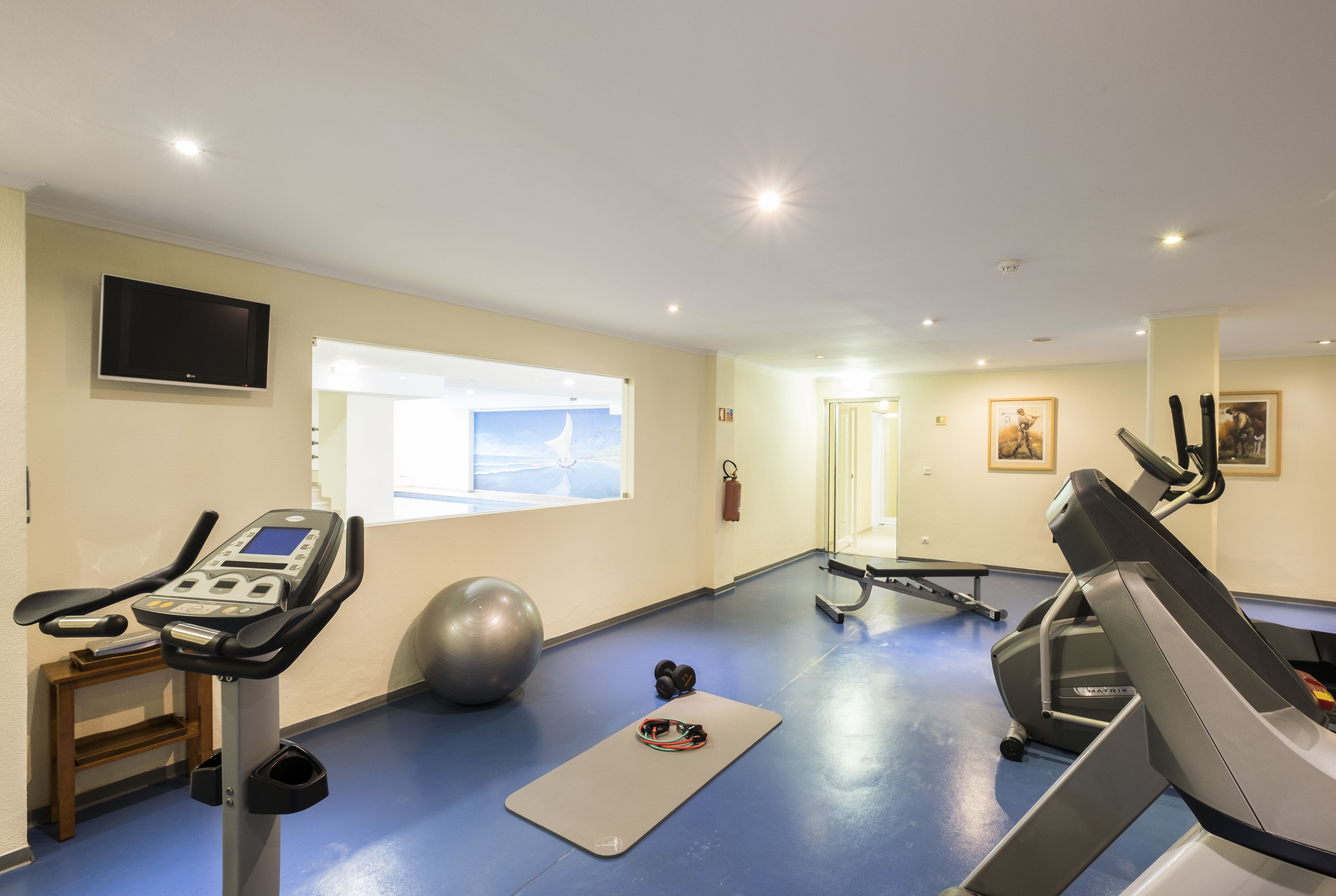 Un gimnasio con equipo de ejercicio, una cinta de correr, una bicicleta estática y una pelota grande.