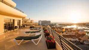 Eine Dachterrasse mit Liegestühlen und Blumenkästen mit Blick auf einen Yachthafen und Gebäude.