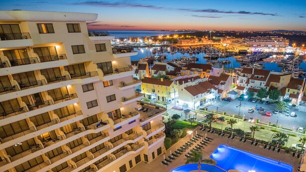 Ein Hotel mit mehreren Etagen, einem zentralen Innenhof mit Swimmingpool und einer Marina im Hintergrund.