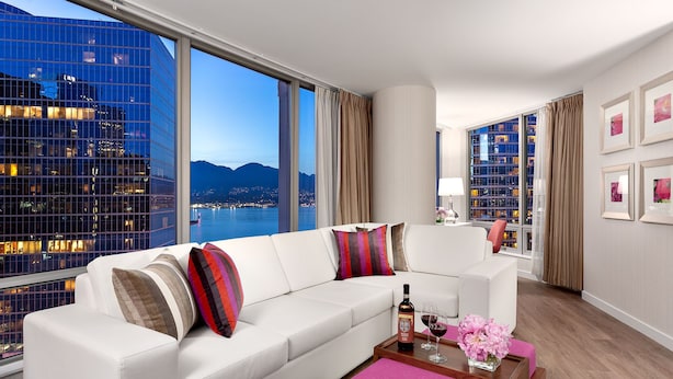 A modern living room with a white sofa, a wooden coffee table, and a city view through large windows. - Auberge Vancouver Hotel (Vancouver)