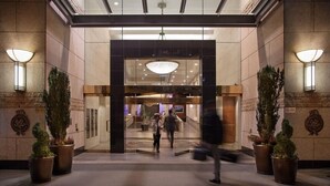 A hotel entrance with a glass facade, potted plants, and a modern interior. - Auberge Vancouver Hotel (Vancouver)