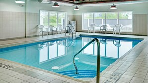 An indoor swimming pool with clear blue water, tiled walls, and a poolside area with white chairs.