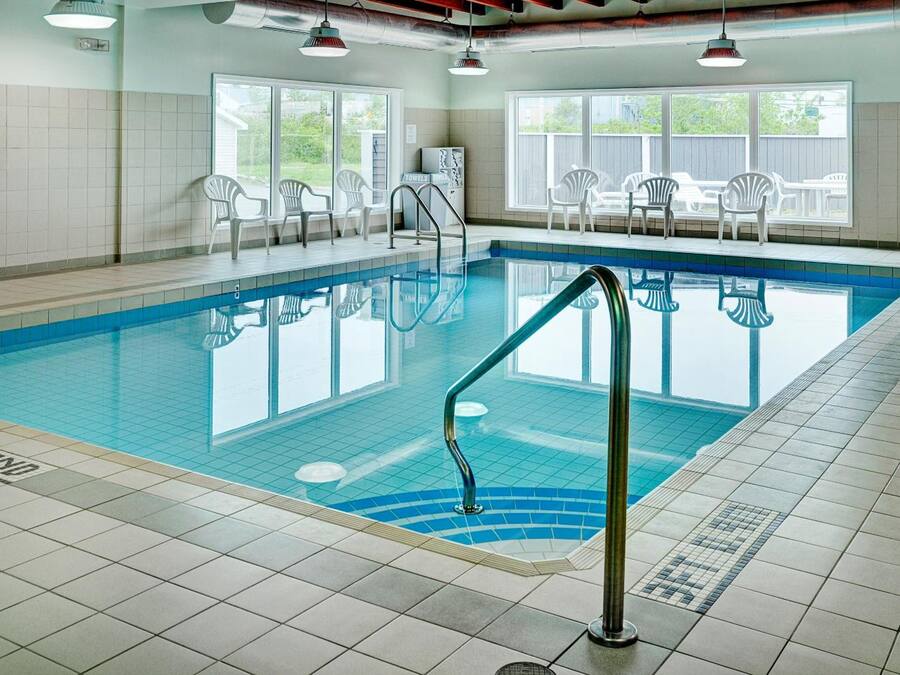 An indoor swimming pool with clear blue water, tiled walls, and a poolside area with white chairs.