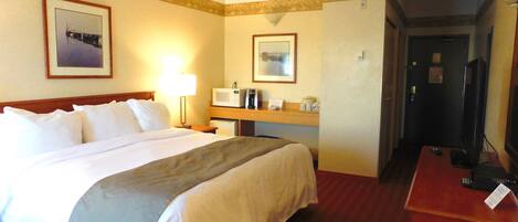 A hotel room with a large bed, a bedside table with a lamp, a microwave, and a television.