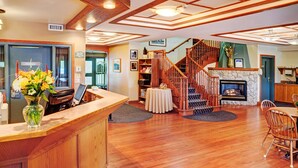 A reception area with a wooden counter, a vase of flowers, a staircase, a fireplace, and a dining area with chairs.