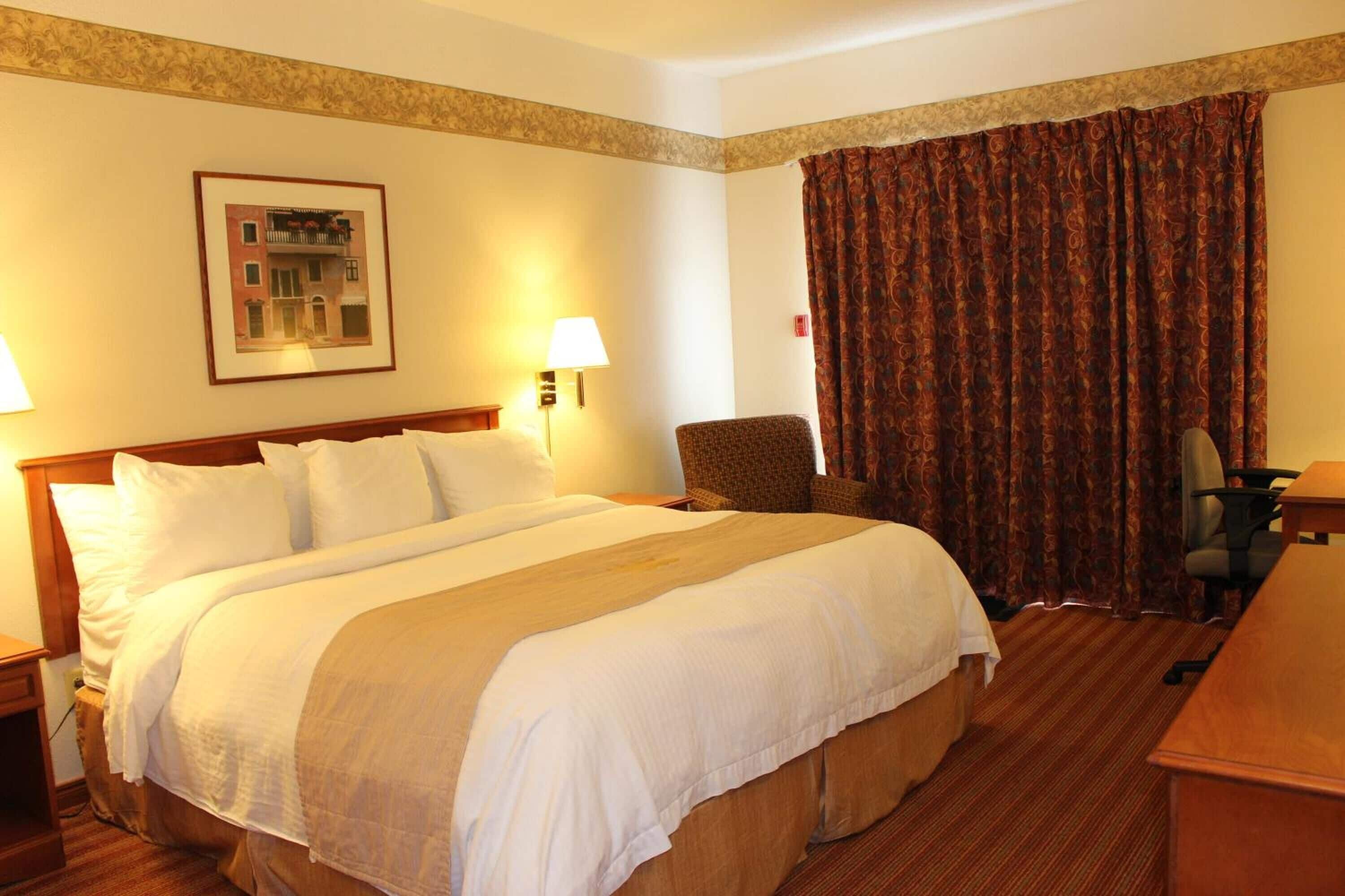A hotel room with a large bed, a chair, a desk, and a curtain.