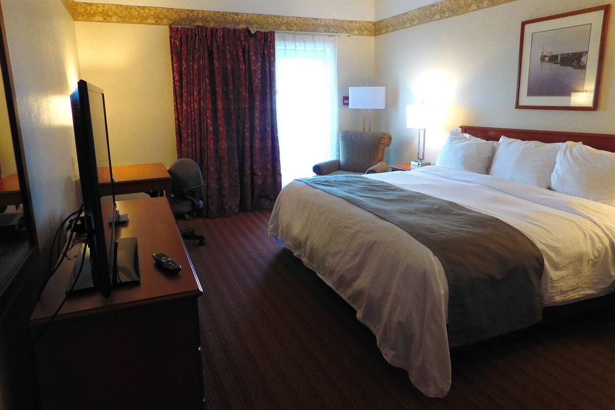 A hotel room with a large bed, a desk with a television, a chair, and a window with curtains.
