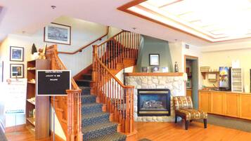 A staircase with wooden railings leading to a landing, a stone fireplace, and a reception desk with a sign.