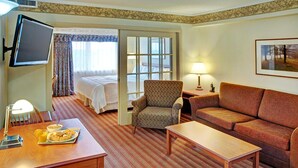 A hotel room with a bed, a sofa, a chair, a TV, a table with breakfast, and a window with curtains.