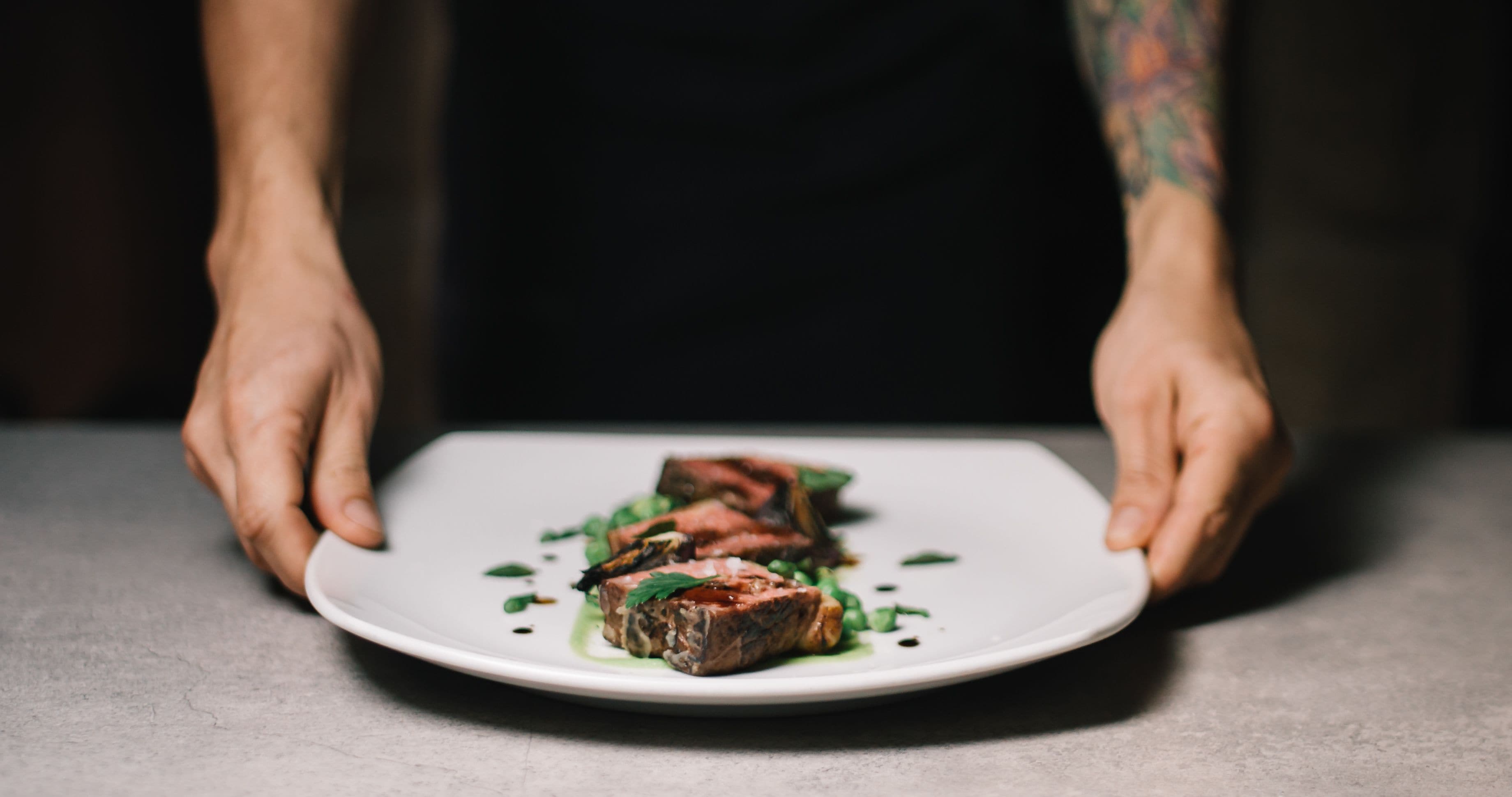 A white plate with steak and greens on a table.