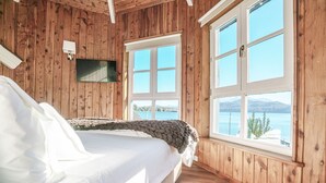 Une chambre à coucher aux murs lambrissés, dotée d’un grand lit, de deux fenêtres et offrant une vue sur un lac.