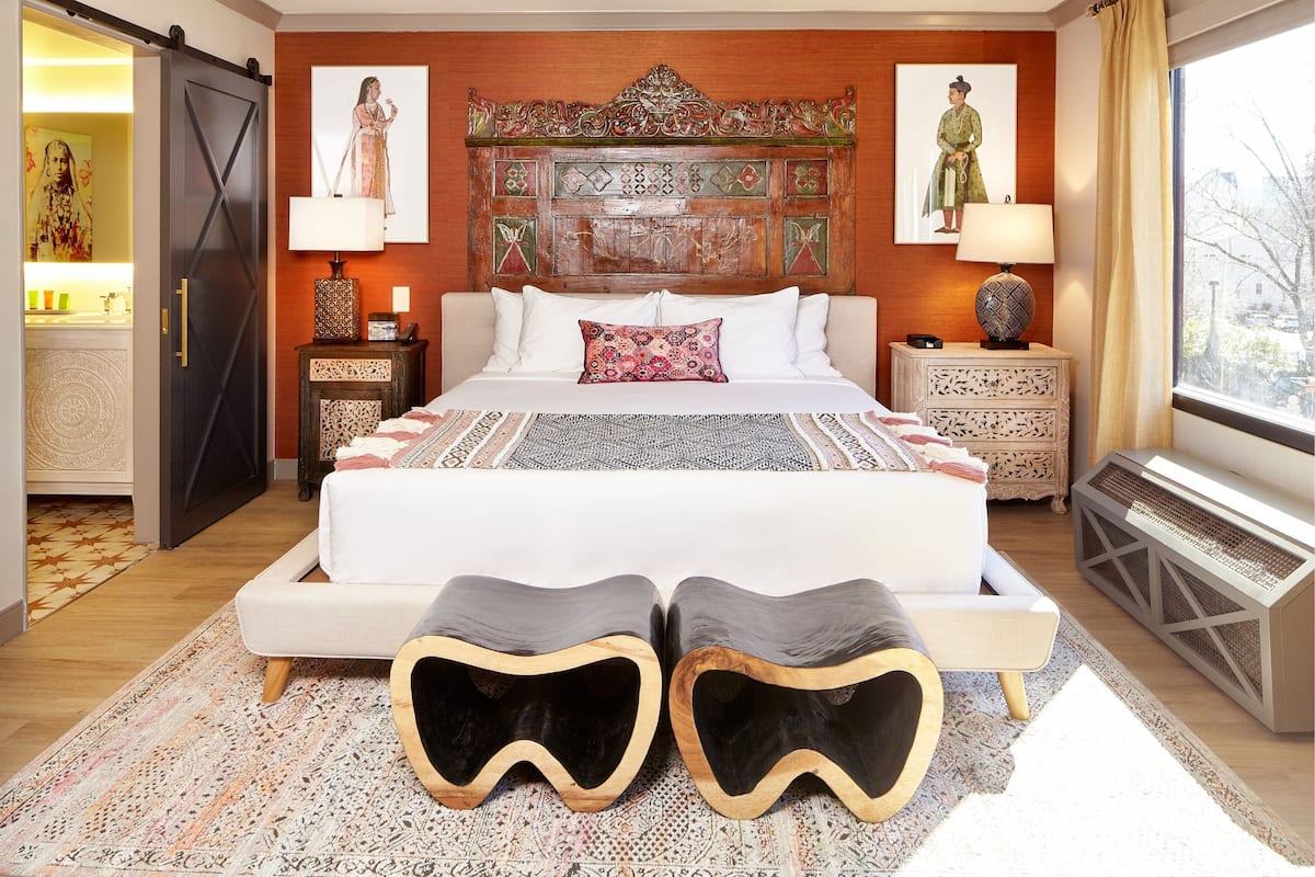 A bedroom with a large bed, two nightstands, a decorative headboard, and a view of the outside through a window.