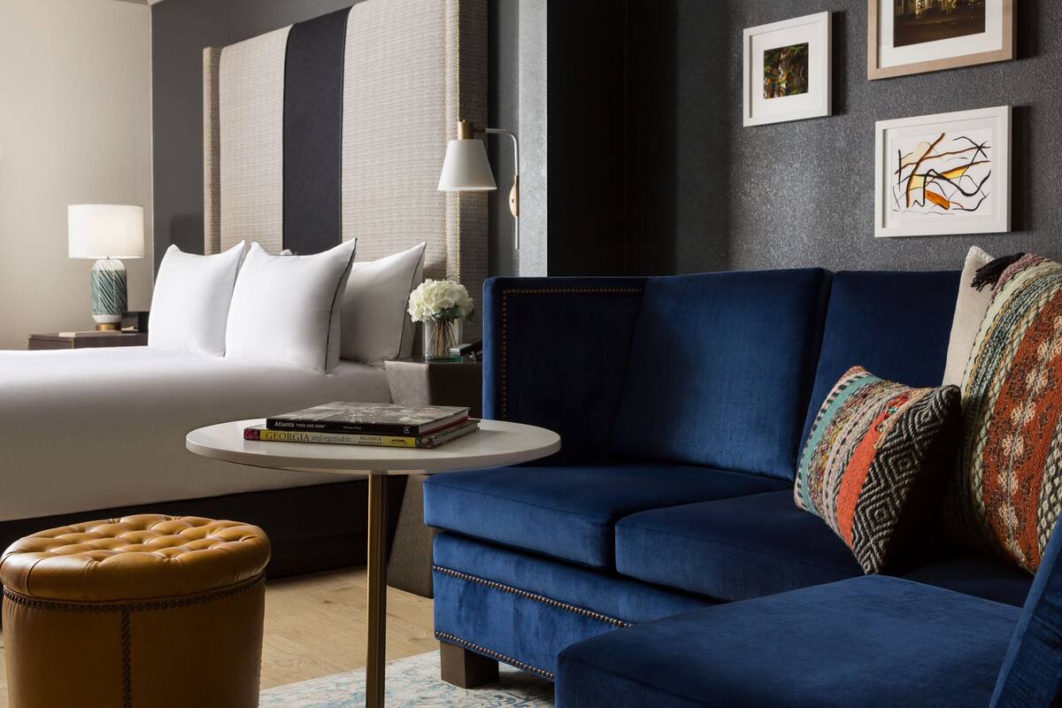 A modern hotel room with a large bed, a blue sofa, a small round table, and a decorative wall with framed pictures.