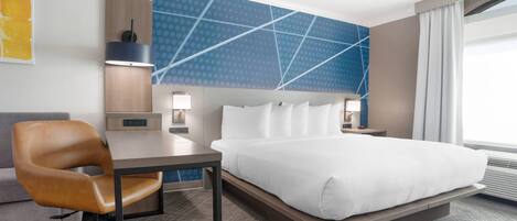 A hotel room with a bed, a desk, a chair, a nightstand, and a wall with a geometric pattern.