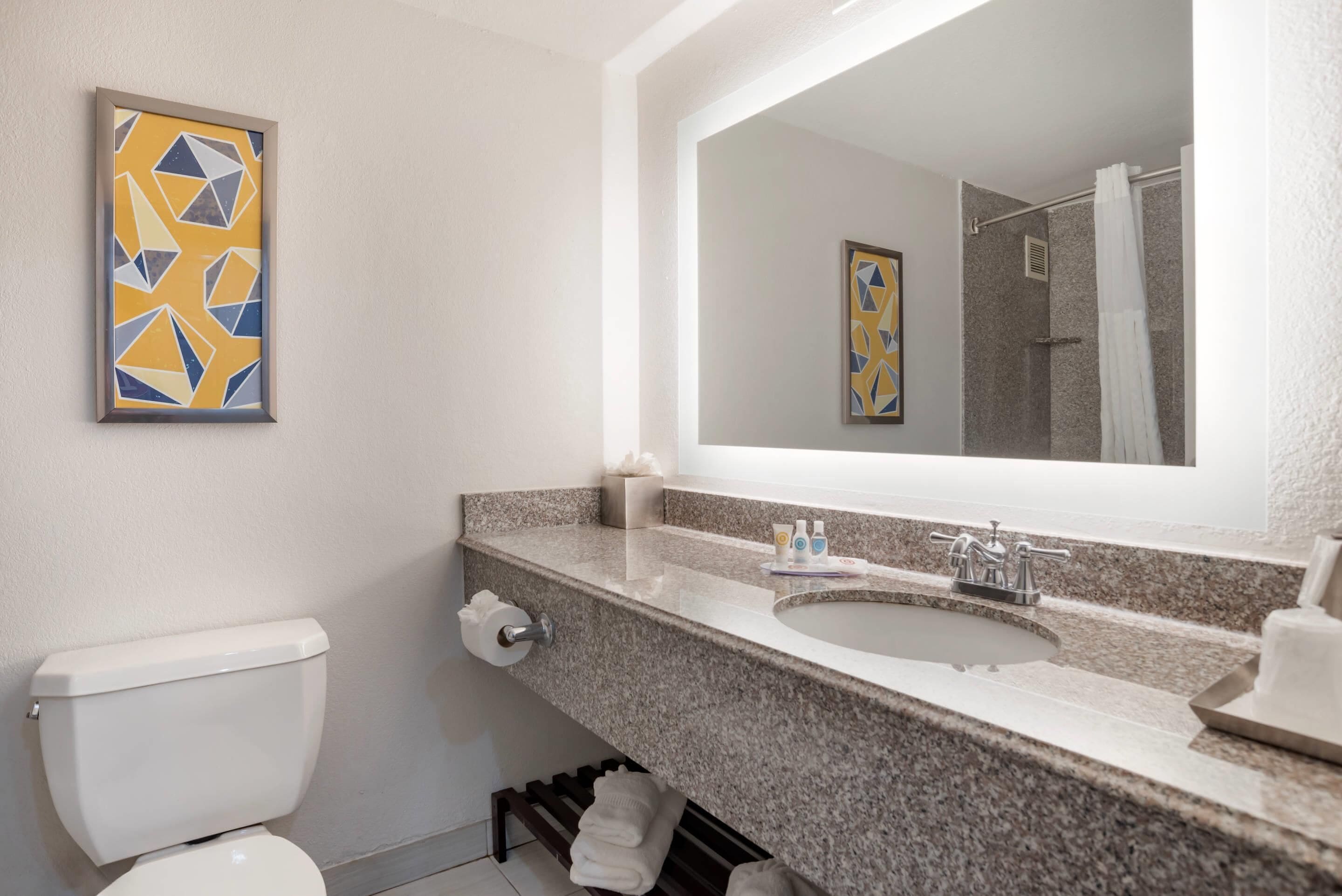 A bathroom with a toilet, sink, and mirror. There are towels and toiletries on the counter.