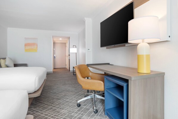 A hotel room with a bed, a desk with a chair, a TV, and a lamp.