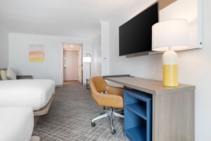 Una habitación de hotel con cama, escritorio con silla, televisor y lámpara.