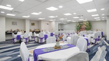 A conference room with round tables, white chairs, and purple sashes.