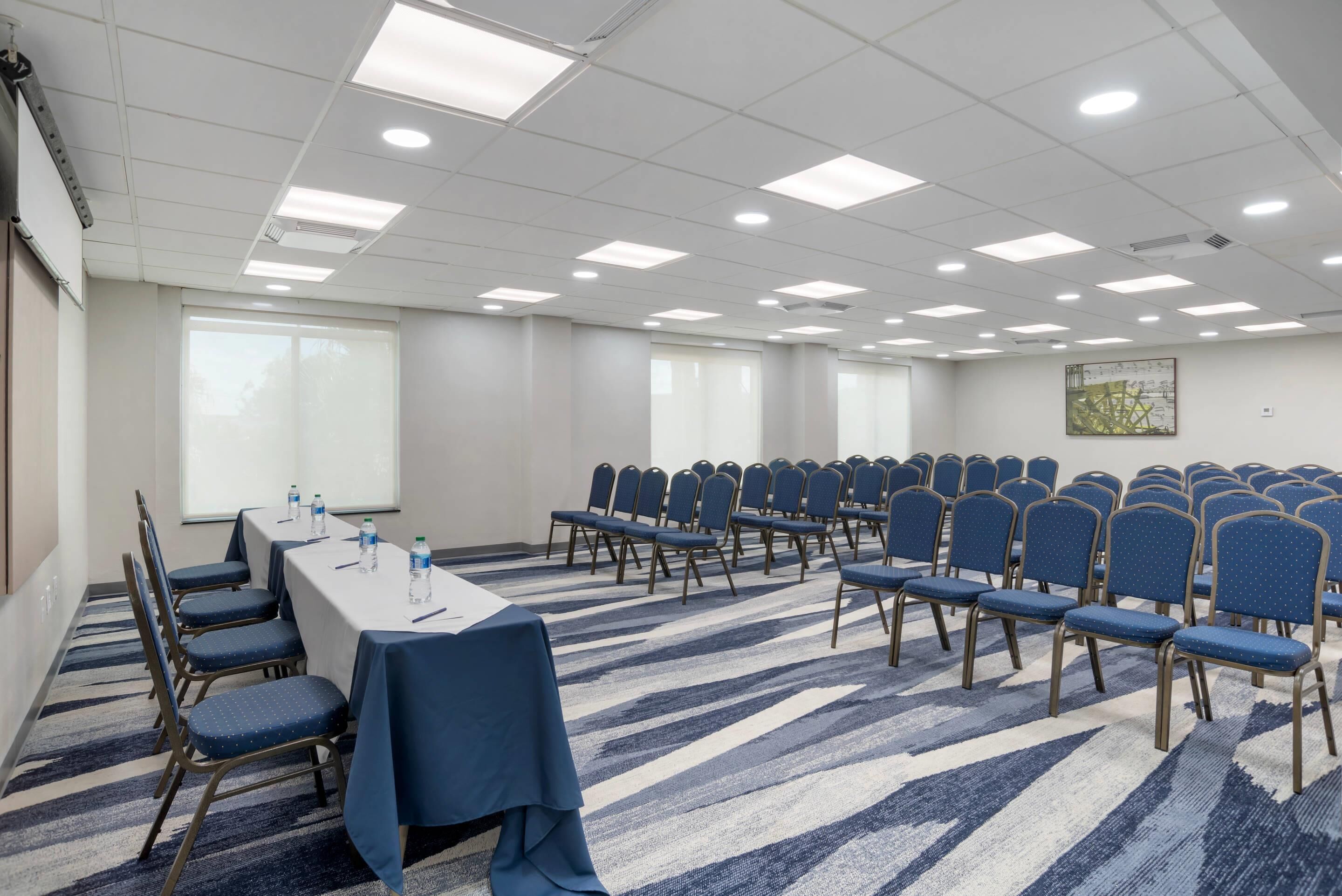 Un salón de conferencias con una larga mesa, filas de sillas y piso alfombrado.