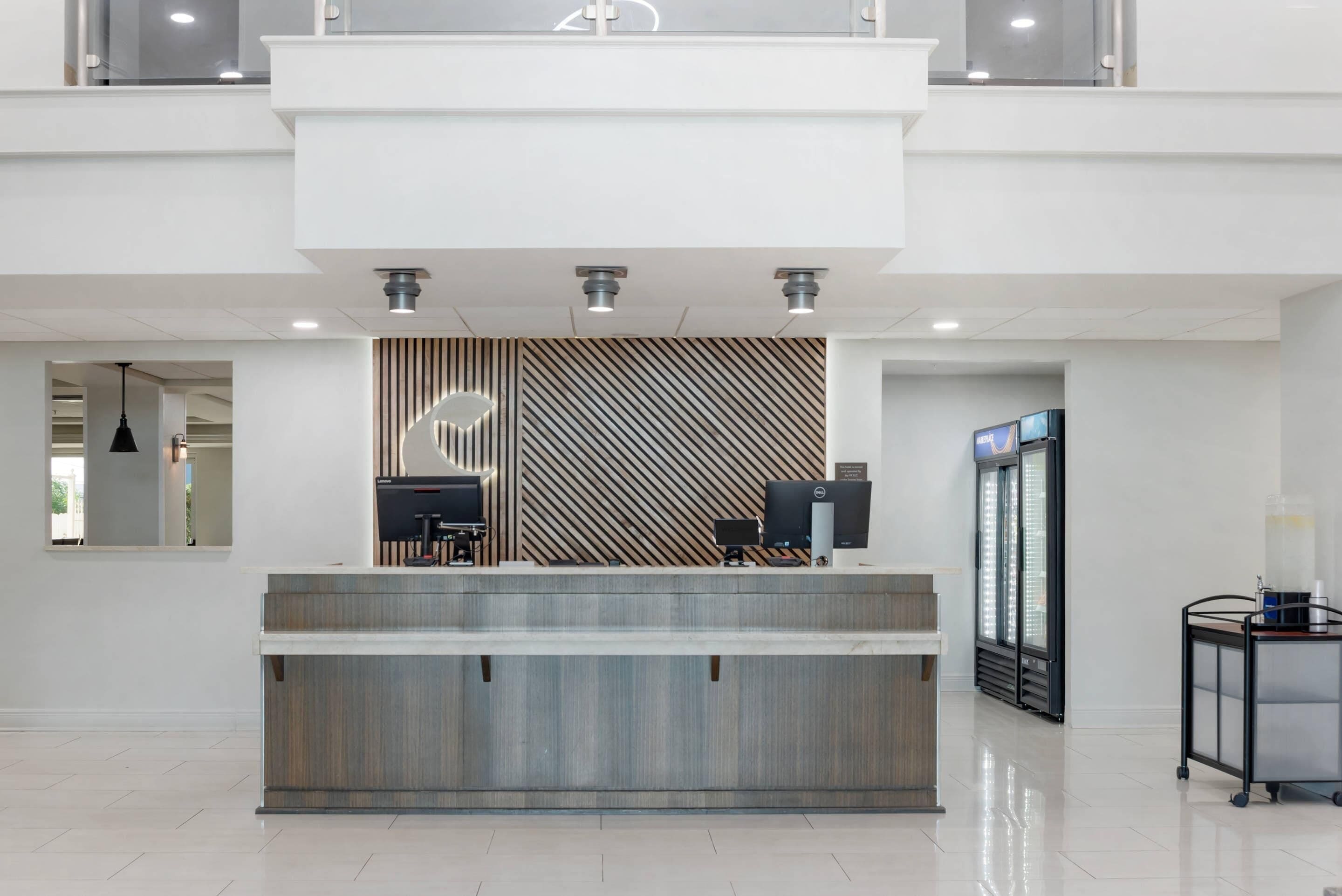 A reception desk with a modern design, a flat-screen monitor, a desktop computer, and a refrigerator.