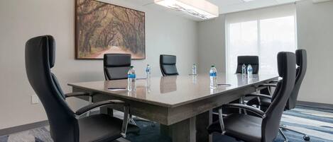 Uma sala de conferência com uma grande mesa, seis cadeiras, garrafas de água e um quadro na parede.