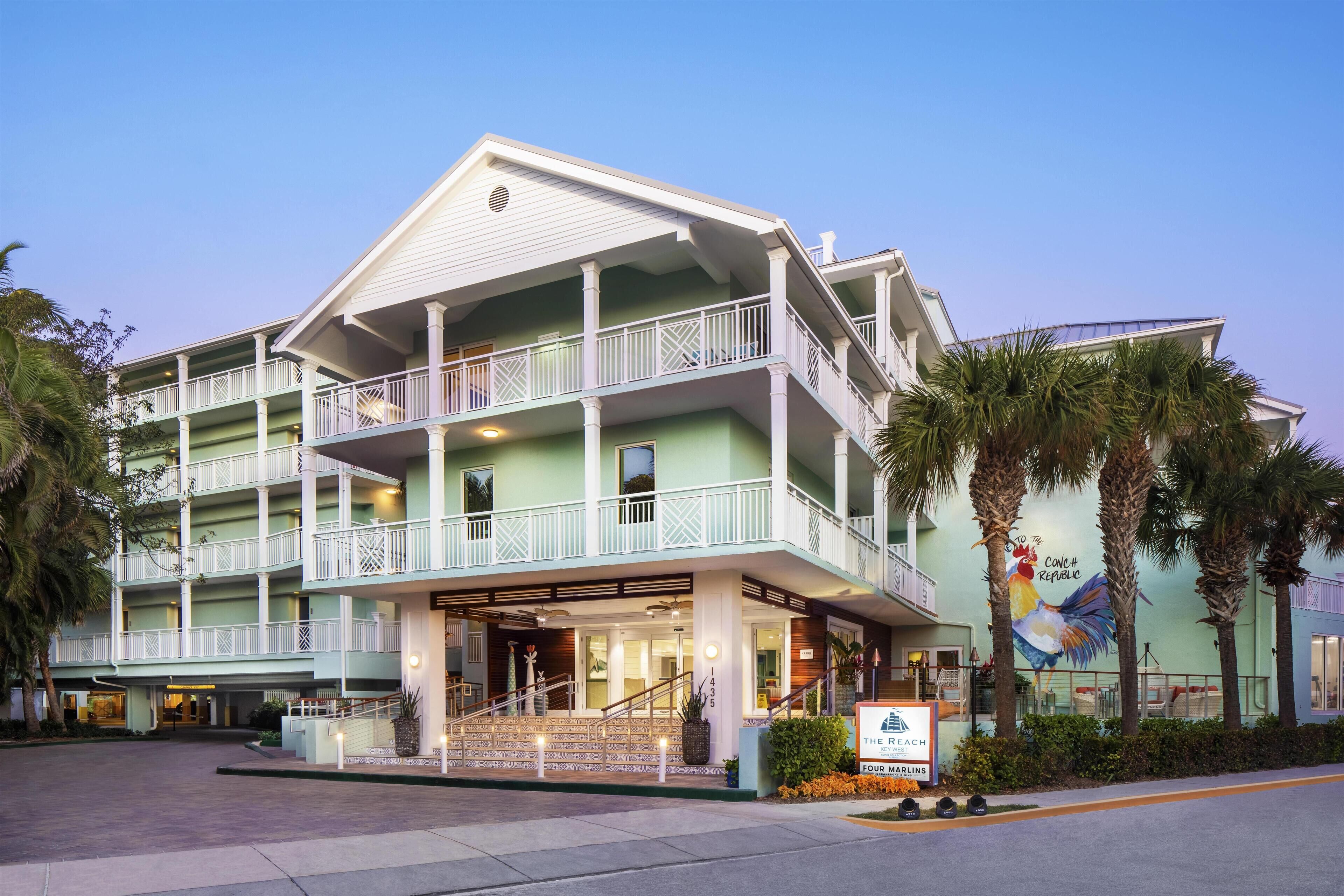 A multi-story hotel with balconies, a central entrance, and a mural of a rooster.