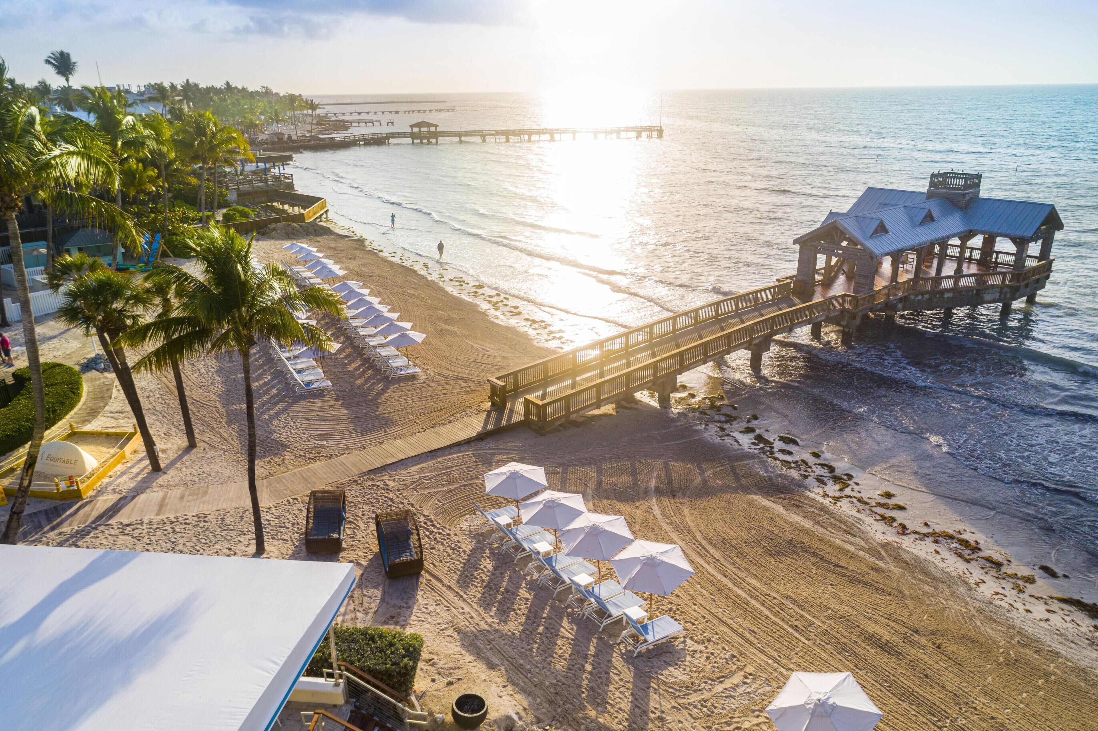 A beach with a wooden pier, beach umbrellas, and lounge chairs.