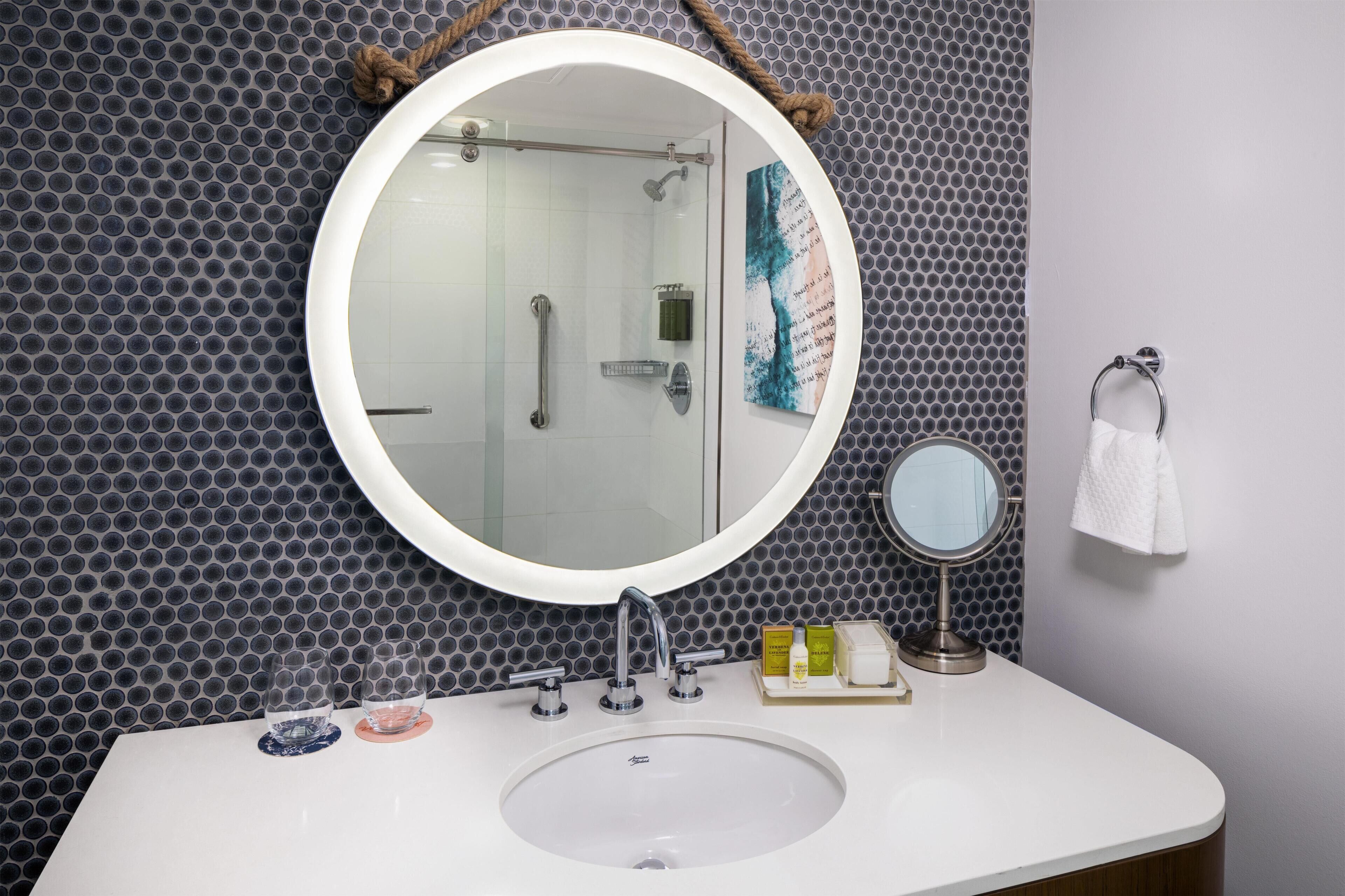 Une salle de bain avec un miroir rond, un lavabo et une douche.