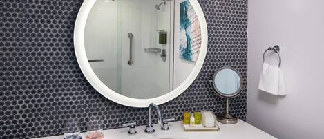 Une salle de bain avec un miroir rond, un lavabo et une douche.