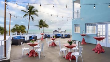 A rooftop bar with white chairs and tables, string lights, and a view of the ocean.