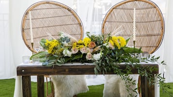 Una mesa con un centro de flores, dos sillas de mimbre y un reposapiés blanco y mullido.