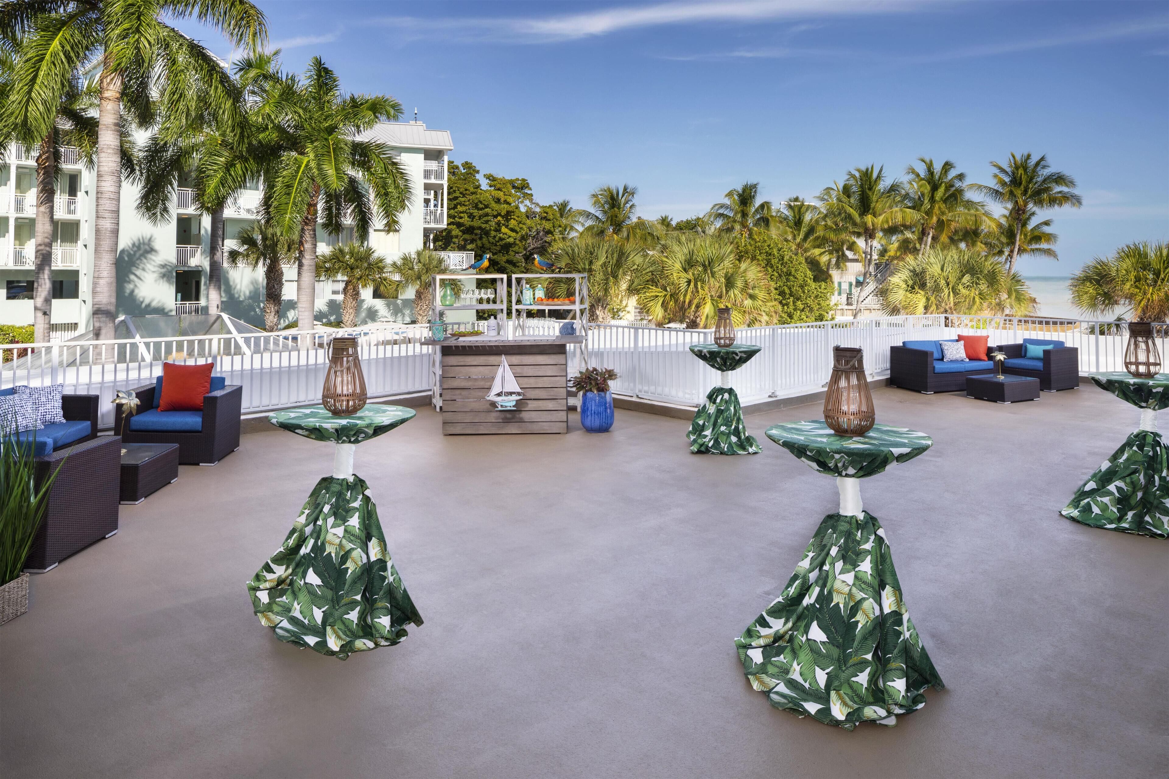 Un área de lounge en la azotea con asientos al aire libre, palmeras y vista al océano.