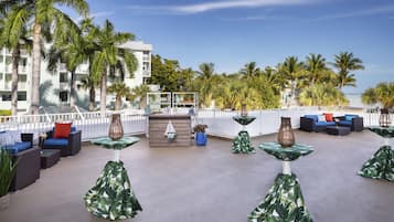 Un área de lounge en la azotea con asientos al aire libre, palmeras y vista al océano.
