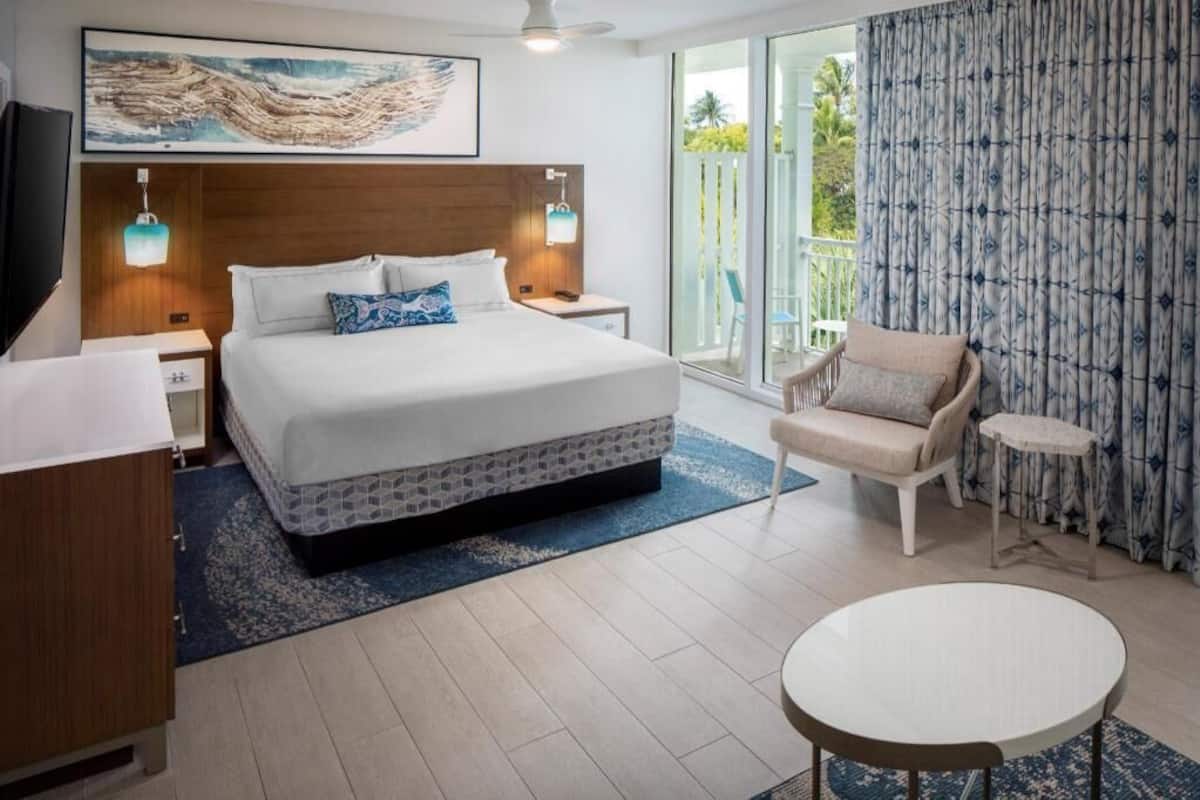 Een moderne hotelkamer met een groot bed, een zithoek met een stoel en een tafel, een televisie en een balkon met gordijnen.