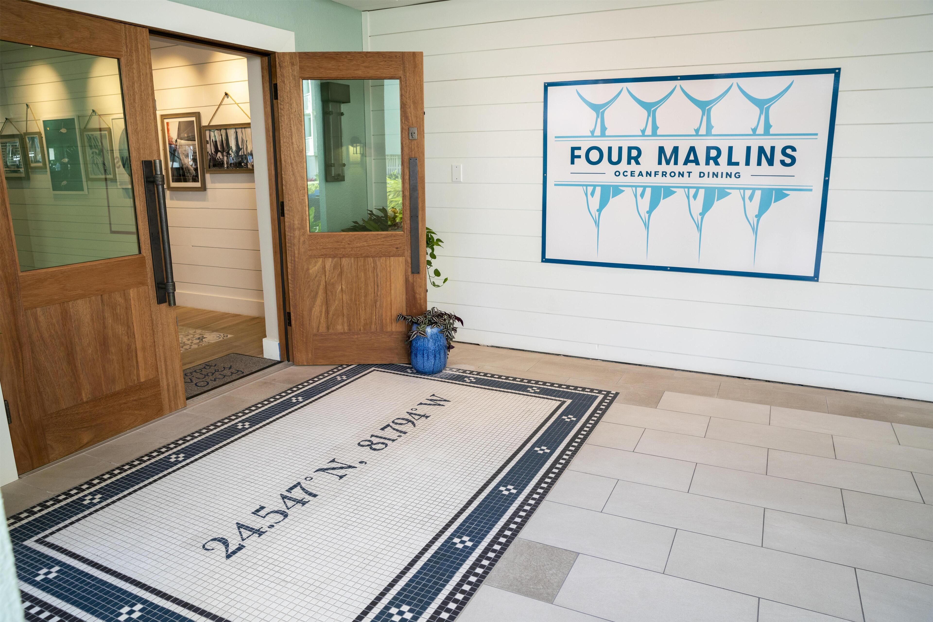 A hotel entrance with a wooden door, a welcome mat with a number, and a sign for 'Four Marlins Oceanfront Dining'.